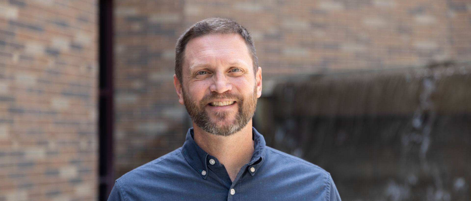 Matt Mason smiling in front of brick building and fountain